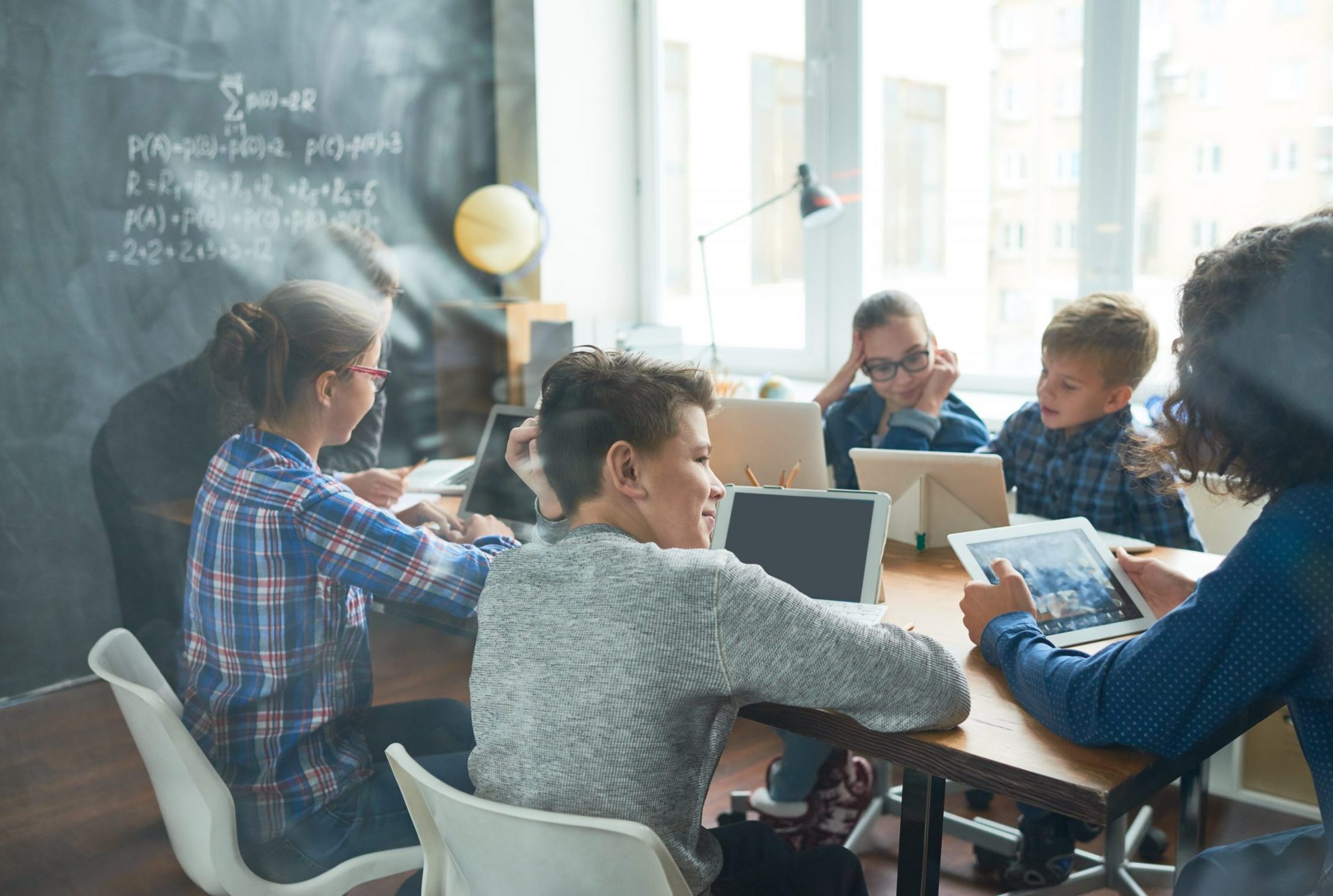 Group of modern students using gadgets while brainstorming together with teacher at class